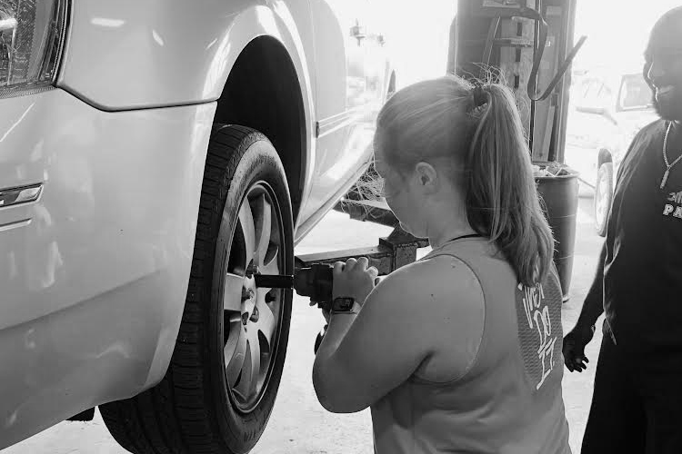 Student uses drill on car wheel rim